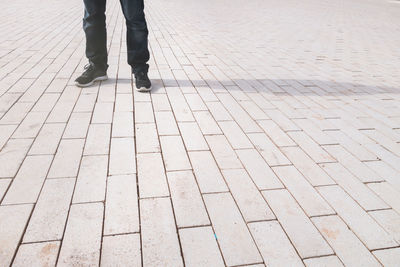 Low section of man standing on footpath during sunny day