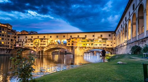 Low angle view of ponte vecchio over arno river against cloudy sky