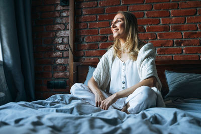 Portrait of young woman sitting on bed at home