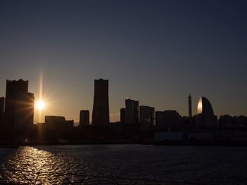 Silhouette buildings by river against sky during sunset