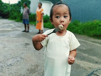 Baby girl having food while standing on road