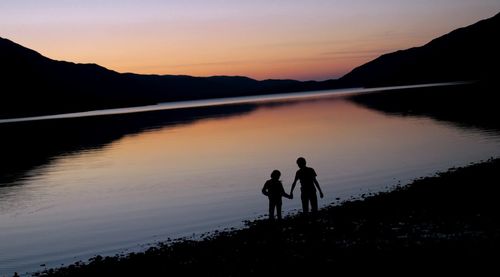 High angle view of silhouette children standing at lakeshore during sunset