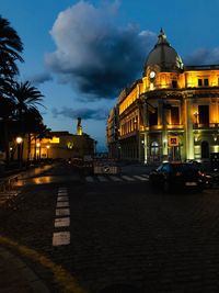 Cars on road by illuminated buildings against sky at dusk