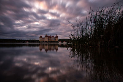 Reflection of building in lake against sky at sunset