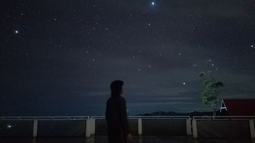 Rear view of silhouette man standing against sky at night