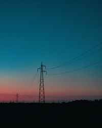 Low angle view of electricity pylon against clear sky during sunset
