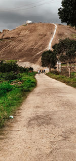 Dirt road amidst trees against sky