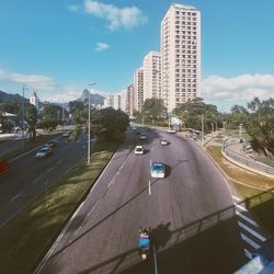 Cars on road by buildings in city against sky