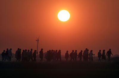 Silhouette people on landscape against orange sky