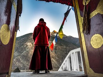 Rear view of monk standing on cross against mountain