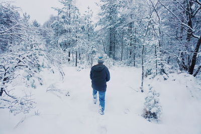 Rear view of man walking on snow covered forest