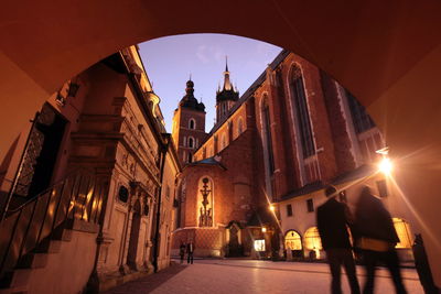 Rear view of people walking on street by tunnel against wawel cathedral at dusk
