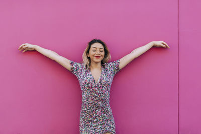 Smiling woman with arms outstretched leaning on wall