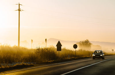 Car on road against sunrise sky during foggy summer morning