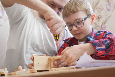 Father helping son with screwdriver to build model airplane at home