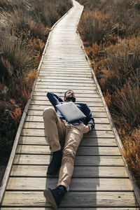 High angle view of mid adult man with laptop lying on boardwalk