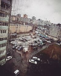 High angle view of city buildings seen through wet window