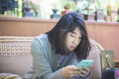 Young woman using mobile phone while sitting on sofa at home