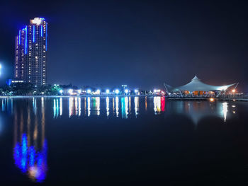 Illuminated city by sea against sky at night