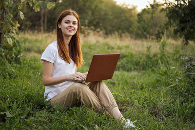 Portrait of young woman using digital tablet while sitting on field