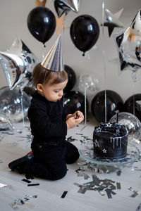 Boy stands next to a festive black cake and balloons