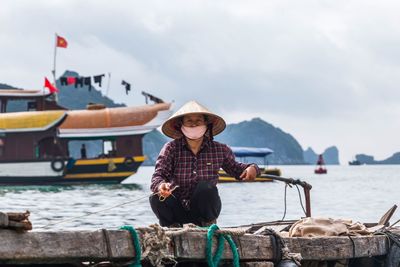 Young woman sitting on boat in river against sky