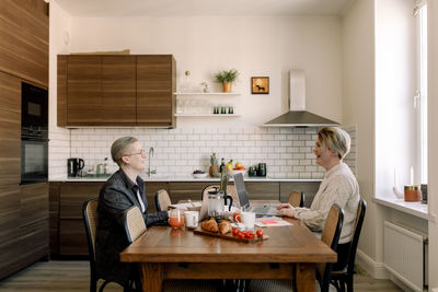 Young lesbian couple talking to each other while sitting at dining table in kitchen