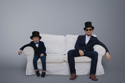 Full length portrait of friends sitting against gray background