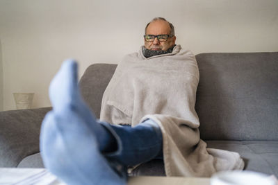 Senior man wrapped in blanket sitting on sofa at home