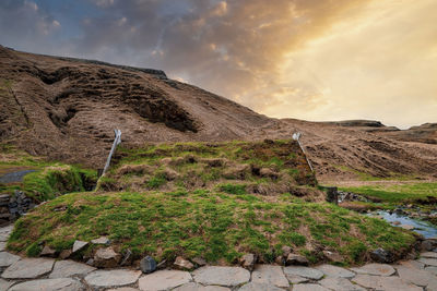 View of turf house and geothermal hot pot in hrunalaug on mountain against sky