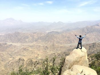 Rear view of man standing on rock against sky