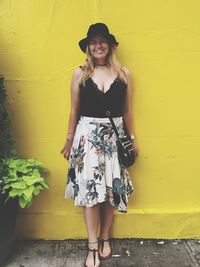 Full length of happy woman standing against yellow wall