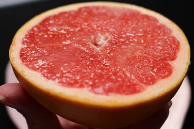 Close-up of hand holding sliced grapefruit 