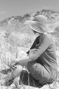 Rear view of woman sitting on the beach using hat