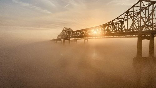 Illuminated bridge over river against sky during sunset