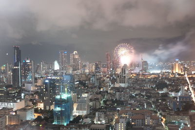 Firework exploding over illuminated cityscape against sky