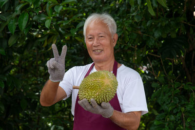 Man holding durian while standing against trees