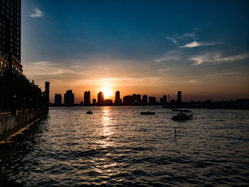 Silhouette buildings by sea against sky during sunset