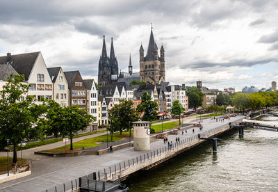 Buildings by river against cloudy sky