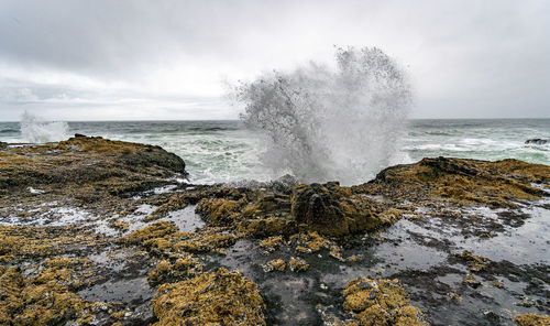 Sea waves splashing on rocks against sky