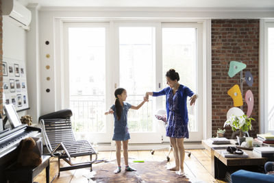 Girl and mother holding hands and dancing on carpet at home