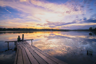 Man sitting on jetty against sky during sunset