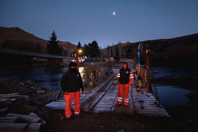 Rear view of man standing on lake against sky at night