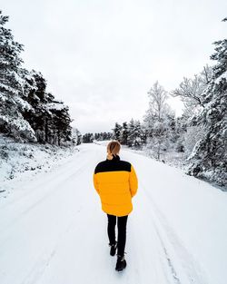 Rear view of woman walking on snow covered road during winter