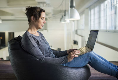 Side view of mature businesswoman using laptop while sitting on bean bag in office