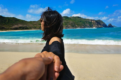 Cropped image of man holding woman hand at beach