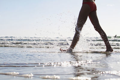 Low section of woman splashing water in sea against sky