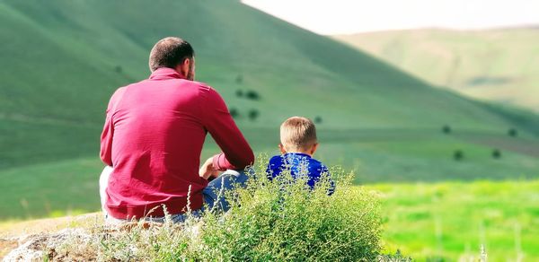 Rear view of father with son sitting on field