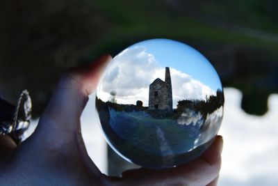 Close-up of hand holding crystal ball against sky