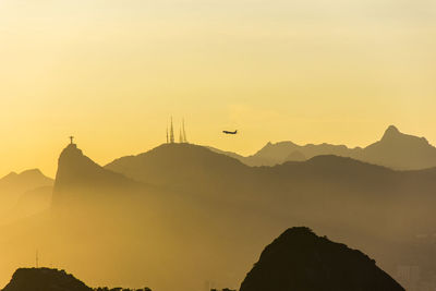 Silhouette birds flying over mountains against sky during sunset